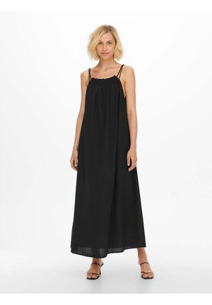 Robe maxi noire en tissu texturé avec un col froncé et des bretelles fines, descendant jusqu'aux chevilles, associée à des sandales à lanières.