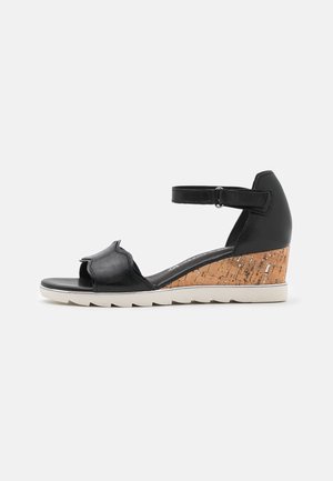 Sort kile-sandal med ankelrem, åben tå og korktekstureret hæl på hvid baggrund.