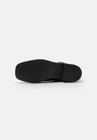 Suela de zapato negra con una forma suave y redondeada, que presenta ranuras horizontales para tracción y un área de talón ligeramente elevada.