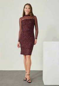 Robe bordeaux ornée de sequins avec des manches longues transparentes et une silhouette ajustée, mettant en avant un col haut et un design jusqu'aux genoux.