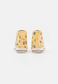 Gula högskor med färgglada mönster av bokstäver och symboler, med en vadderad krage och en kontrasterande svart gummisula.