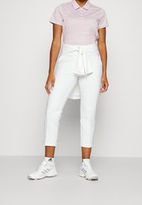 Ljusrosa randig pikétröja med korta ärmar, i kombination med högmidjade vita byxor som har en knytaccent och kort längd. Vita sneakers.