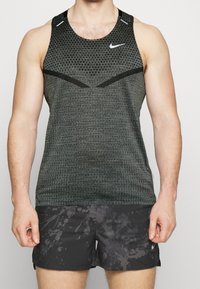 Débardeur Nike gris foncé avec un motif texturé, présentant des accents noirs et des détails réfléchissants. Porté avec un short noir arborant un design éclaboussé.