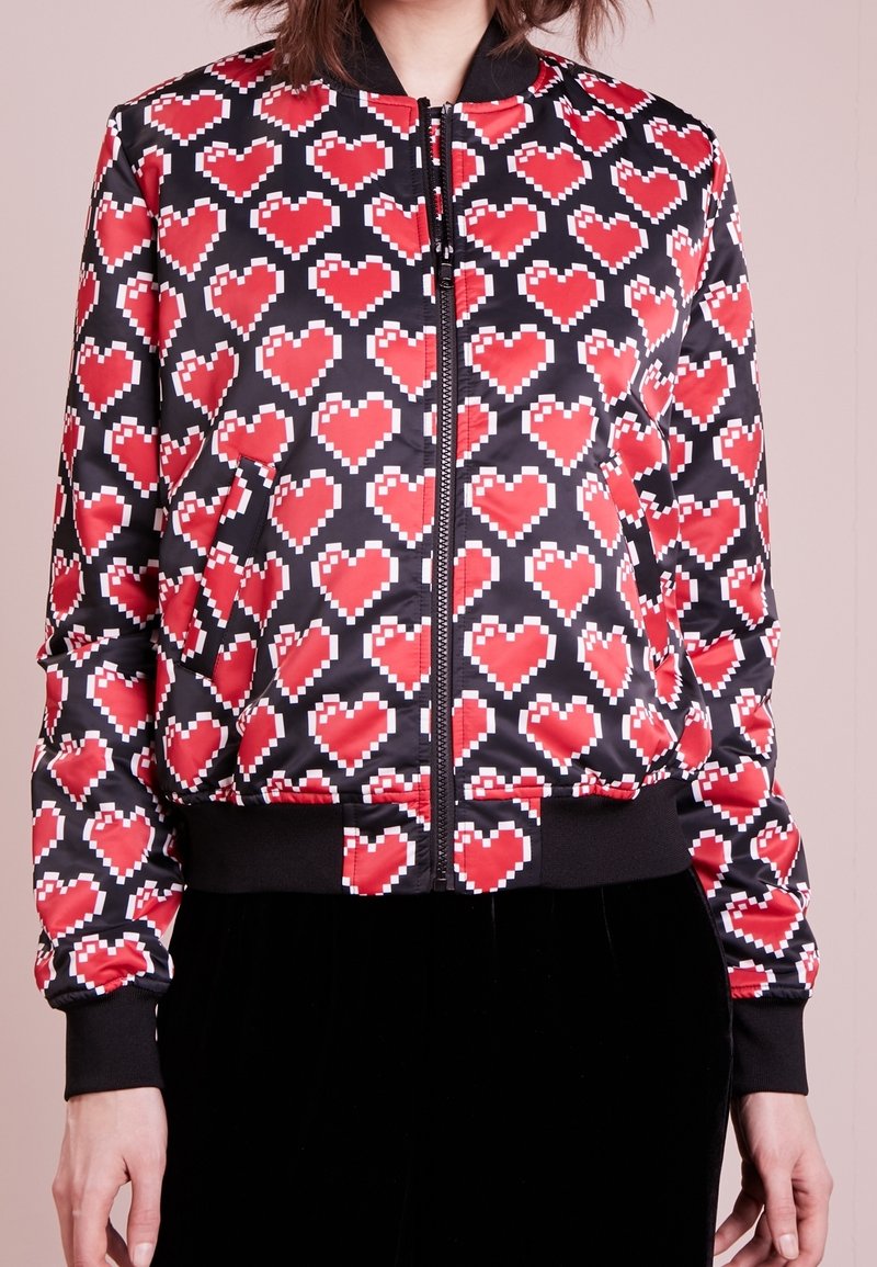 Black bomber jacket featuring red pixelated heart patterns, zip closure, ribbed cuffs, and waistband in a glossy, smooth fabric.