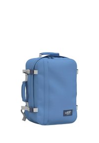 Zaino da viaggio blu con una superficie liscia, molteplici cerniere, maniglia laterale, spallacci regolabili e un'etichetta con logo nell'angolo inferiore.