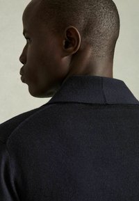 Polo de punto navy con cuello acanalado. Presenta una textura suave y una silueta estructurada, mostrando la espalda y los hombros.