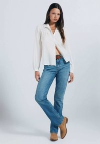 White button-up shirt with long sleeves, blue jeans, and tan ankle boots. The shirt features a loose fit and subtle pleating details.