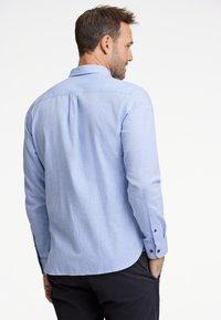 Ljust blå, långärmad skjorta med knappar, bakfålla och knappade ärmslut, tillverkad av ett texturerat tyg, med en rundad fåll.