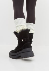Botas de ante negro hasta el tobillo con una suela de goma gruesa, diseño de cordones y borde de piel sintética, combinadas con calcetines blancos de canalé.