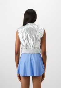 Silberne, verkürzte Jacke mit strukturierten Oberflächen und kurzen Ärmeln, kombiniert mit einem hellblauen, plissierten Rock mit ausgestelltem Saum.