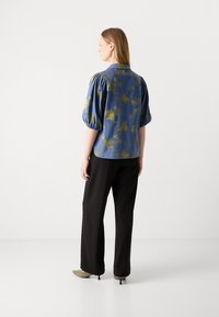 Modra bluzica z motivom in napihnjenimi rokavi, ovratni dizajn in zlatimi cvetličnimi poudarki, v kombinaciji s črnimi širokimi hlačami in bež petami.