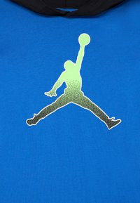 Sweatshirt azul com capuz, apresentando uma grande gráfica verde e preta de uma figura a saltar a segurar uma bola de basquetebol, contra um fundo de tecido liso.