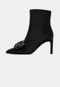 Zwarte enkellaars van glad materiaal, met een spitse neus en naaldhak. Inclusief een stoffen strikdetail aan de voorkant.
