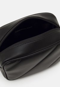 Borsa in pelle nera con superficie texture, dotata di chiusura con zip superiore e etichetta interna che recita "Calvin Klein Jeans."