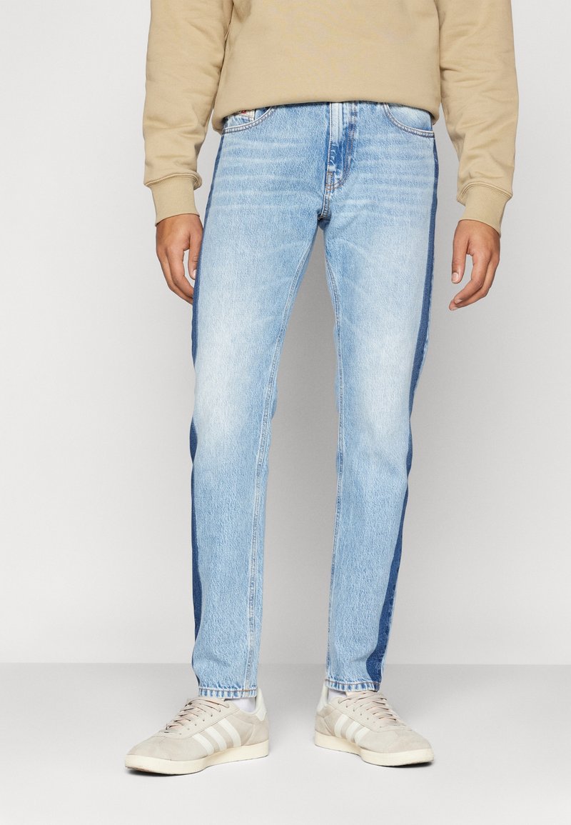 Ljust blå denimjeans med rak passform, som har mörkare sidpaneler, standardfickor och dragkedja, i kombination med beige sneakers.