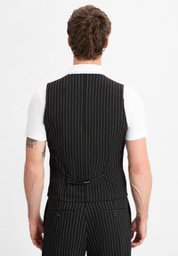 Schwarze, gestreifte Weste mit taillierter Passform, die eine glatte Textur, ein Rückenschnallendetail und ein weißes Hemd mit Kragen darunter aufweist.