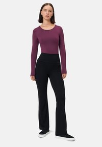 Top a maniche lunghe, aderente, di un profondo colore bordeaux abbinato a pantaloni neri a vita alta e svasati. Tessuto liscio con un design elegante e sneakers nere abbinate.