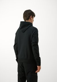 Schwarze Kapuzensweatjacke, weicher Stoff, taillierte Passform, gerippte Bündchen und Saum, glatte Textur, kombiniert mit passenden schwarzen Hosen, minimalistische Optik.