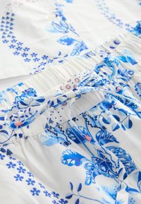 Biely a modrý textil s kvetinovým vzorom, elastickým pásom a detailom stiahnutia na šnúrku.