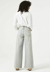 Jeans de lavado claro, de pierna ancha y cintura alta, con dos bolsillos traseros y un corte relajado, combinados con una camisa blanca de botones.