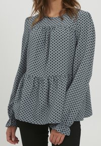 Blusa blu a pois con maniche lunghe, orlo arricciato e tessuto testurizzato; presenta dettagli arricciati lungo il colletto.