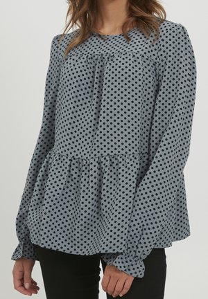 Blaue Bluse mit Punkten, langen Ärmeln, gerüschtem Saum und strukturiertem Stoff; verfügt über geraffte Details am Halsausschnitt.