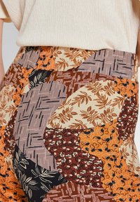 Patroonbroeken met een verscheidenheid aan texturen in oranje, bruin, crème en marineblauw, met bloem- en geometrische patronen. Rekbare tailleband.