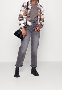 Bunte gemusterte Jacke, graues T-Shirt, hochgeschnittene graue Jeans und schwarze Combat-Stiefel. Eine schwarze Handtasche mit Kettenriemen rundet das Outfit ab.