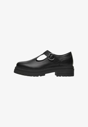 Chaussure en cuir noire avec un bout rond, un design découpé, une bride de cheville et une boucle en argent. Elle dispose d'une semelle épaisse et texturée pour une meilleure adhérence.