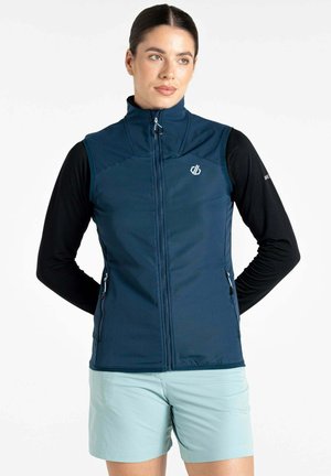Marineblauer Softshell-Weste mit hohem Kragen, Frontreißverschluss und Seitentaschen. Getragen über einem schwarzen Langarmoberteil, kombiniert mit hellen Shorts.