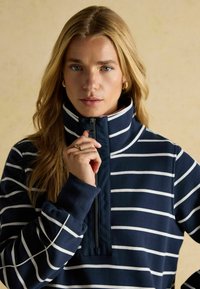 Tumed sinise ja valge triibuline pehme pullover kõrge kaelusega ja neljandiku tõmbluku puhul. Omab mugavat lõiget ja soonikkoes mansette. Pehme materjal.