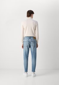 Top de manga larga beige combinado con vaqueros de mezclilla de color azul claro. Los vaqueros tienen un corte recto, dos bolsillos traseros y una etiqueta de cuero marrón en la cintura.