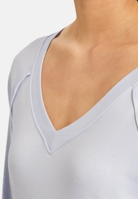 Top azzurro chiaro con scollo a V e maniche lunghe, realizzato in tessuto morbido. Presenta un colletto testurizzato e cuciture affusolate sulle spalle.