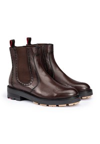 Brown leather ankle boots with elastic side panels, perforated detailing on toe, black sole, and red loop accents at the back.