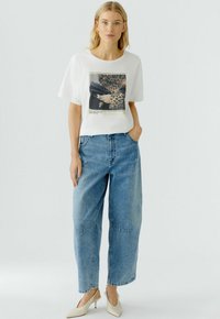 Witte korte mouwen t-shirt met een grafische print, gecombineerd met lichtblauwe denim wijde jeans en beige puntige hakken. Gladde stofstructuur.