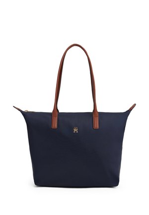 Marineblå tote-taske med brune læderhåndtag og lille gyldent logoemblem centreret under lynlåsen på en hvid baggrund.