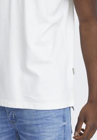 Weißes Baumwoll-T-Shirt mit Rundhalsausschnitt, kurzen Ärmeln und seitlichen Schlitzen. Verfügt über ein kleines Markenetikett am unteren Saum.