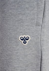 Grau gestreifter Baumwollmix-Stoff mit einer glatten Textur, versehen mit einem gestickten Bienenlogo in Marineblau und Weiß auf der linken Seite.