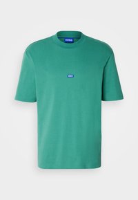 T-shirt vert à manches courtes avec col rond, petit patch rectangulaire bleu "HUGO" centré sur la poitrine.
