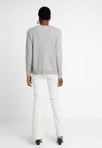 Šedý svetr s volným střihem a padnutými rameny, doplněný bílými rozšířenými džínami a černými kozačkami na podpatku. Jednoduchý, texturovaný design.