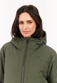 Groene buitenjas met hoge kraag en capuchon, met ritssluiting aan de voorkant en 'protest' logo. Glad, waterafstotend materiaal en een getailleerd ontwerp.
