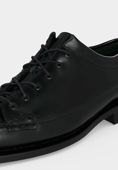 Chaussure formelle en cuir noir avec laçage fermé et finition polie lisse, présentée sur fond blanc.