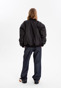 Black puffer jacket with oversized sleeves, ribbed hem, and high collar; paired with dark blue denim pants and black shoes.
