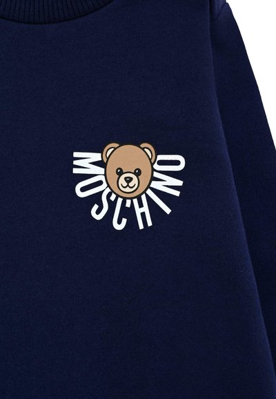 Felpa blu navy con grafica di un orso color beige e il marchio "Moschino" in bianco, posizionati attorno al volto dell'orso. Tessuto morbido, design con scollo a girocollo.