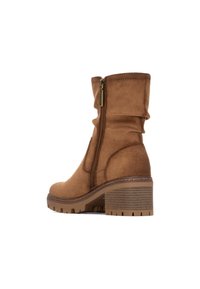 Stivale alla caviglia in suede marrone con design arricciato, chiusura laterale con zip e tacco spesso. Suola texturizzata con un motivo a righe.