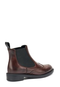 Bota Chelsea de cuero marrón con paneles elásticos a los lados, detalles de brogue en la puntera y un tacón negro apilado para mayor altura.