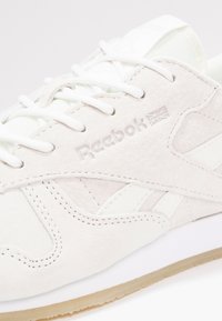 Off-white mockasin Reebok-sneakers med vita snören, sydda detaljer, präglad Reebok-logga och kant med gummisula.