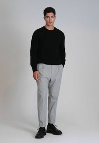 Pull noir à côtes, pantalon ajusté gris clair et chaussures noires à lacets. L'ensemble présente un design simple et moderne avec une coupe décontractée.