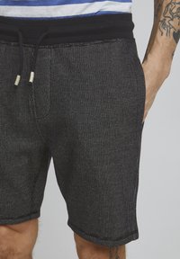Shorts à motifs sombres en matériau léger, dotés d'une taille avec cordon de serrage noir et de poches latérales. Texturés avec de petits points blancs.