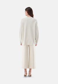 Helles creamfarbenes Oversized-Pullover mit langen Ärmeln, kombiniert mit weit geschnittenen creamfarbenen Hosen. Einfacher, glatter Stoff mit lässiger Passform.